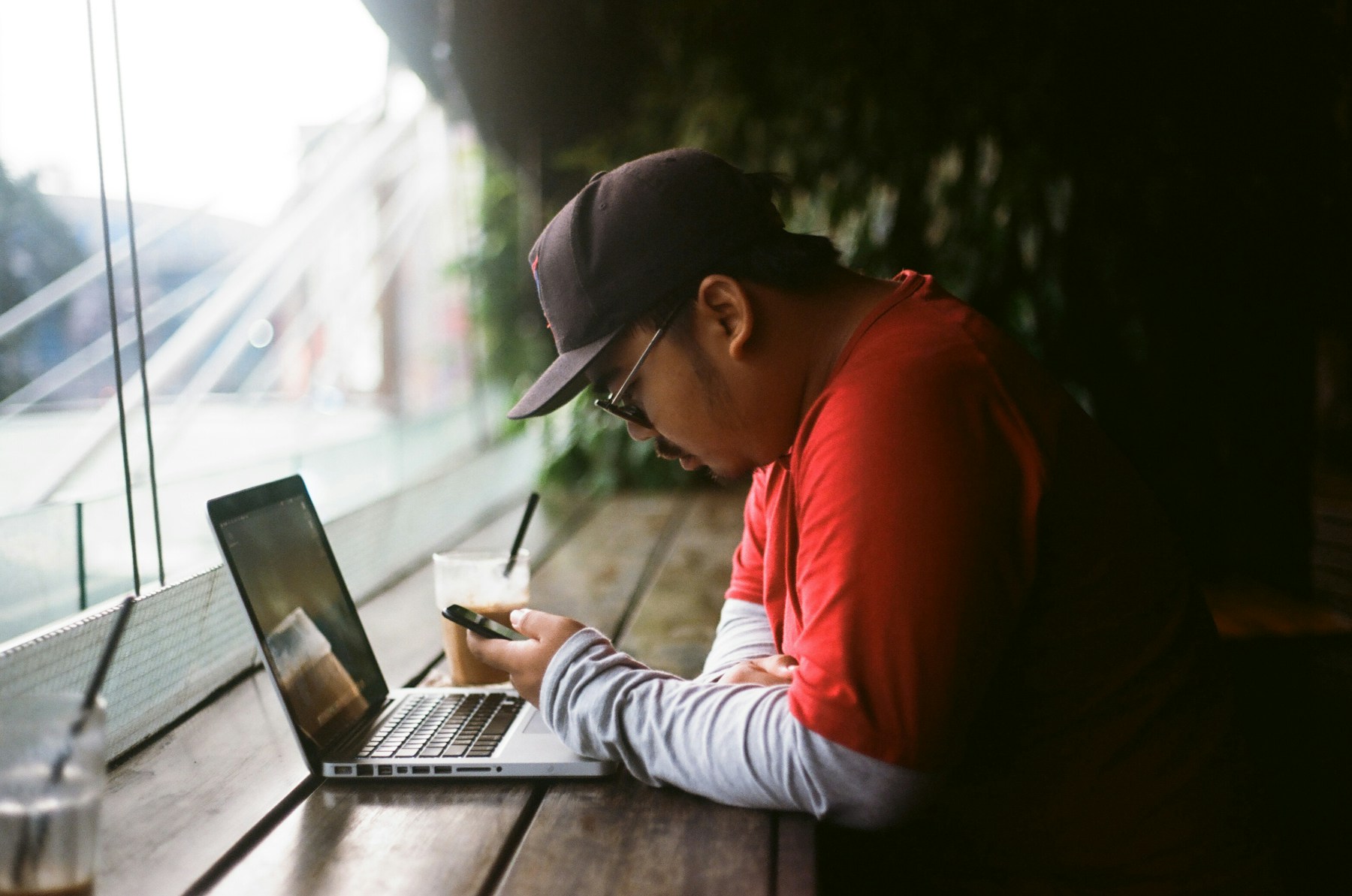 Operator bisnis Indonesia memeriksa pesan pelanggan di ponsel sambil membuka laptop