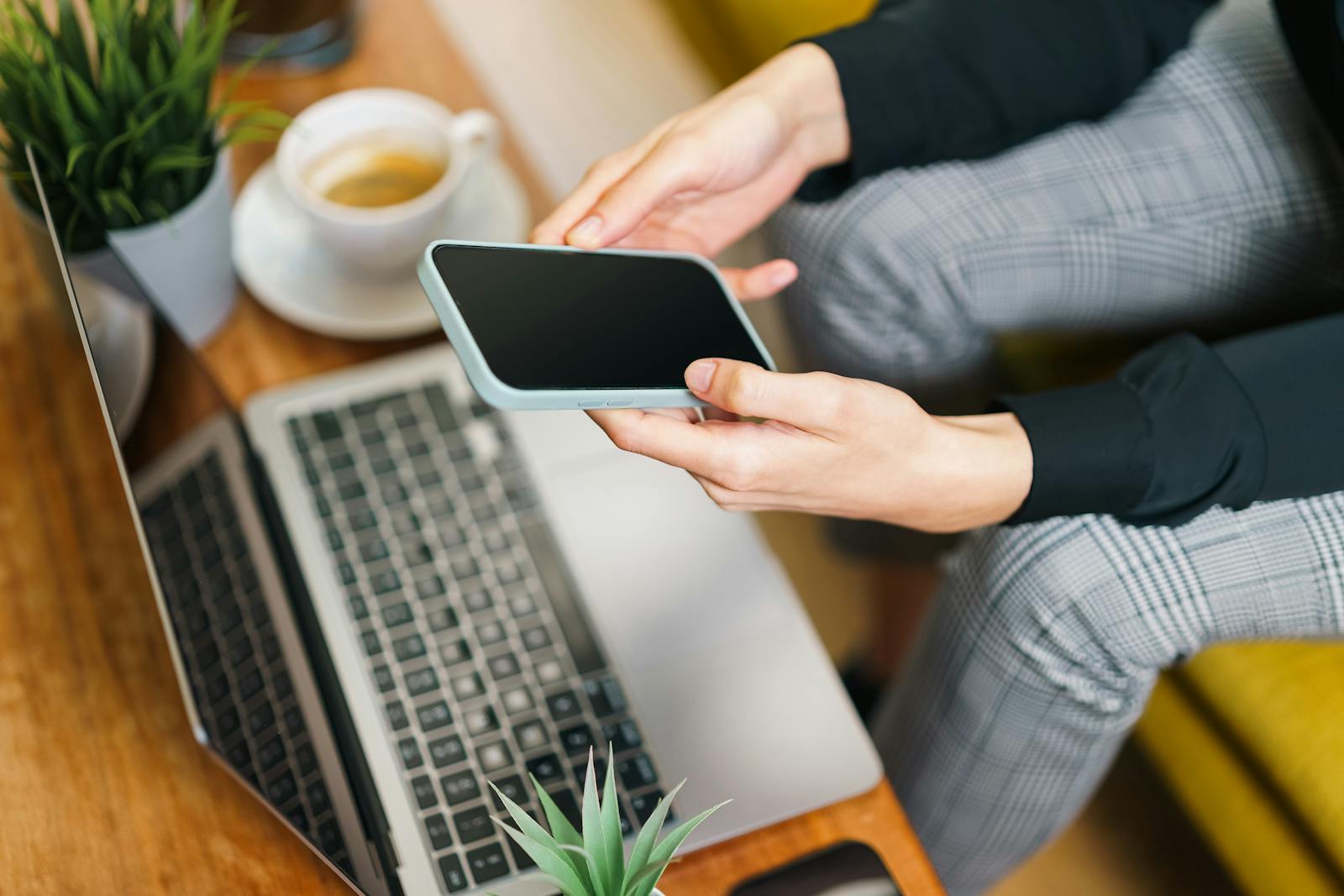 Pemilik bisnis mengecek akses website melalui laptop dan ponsel di meja kerja.