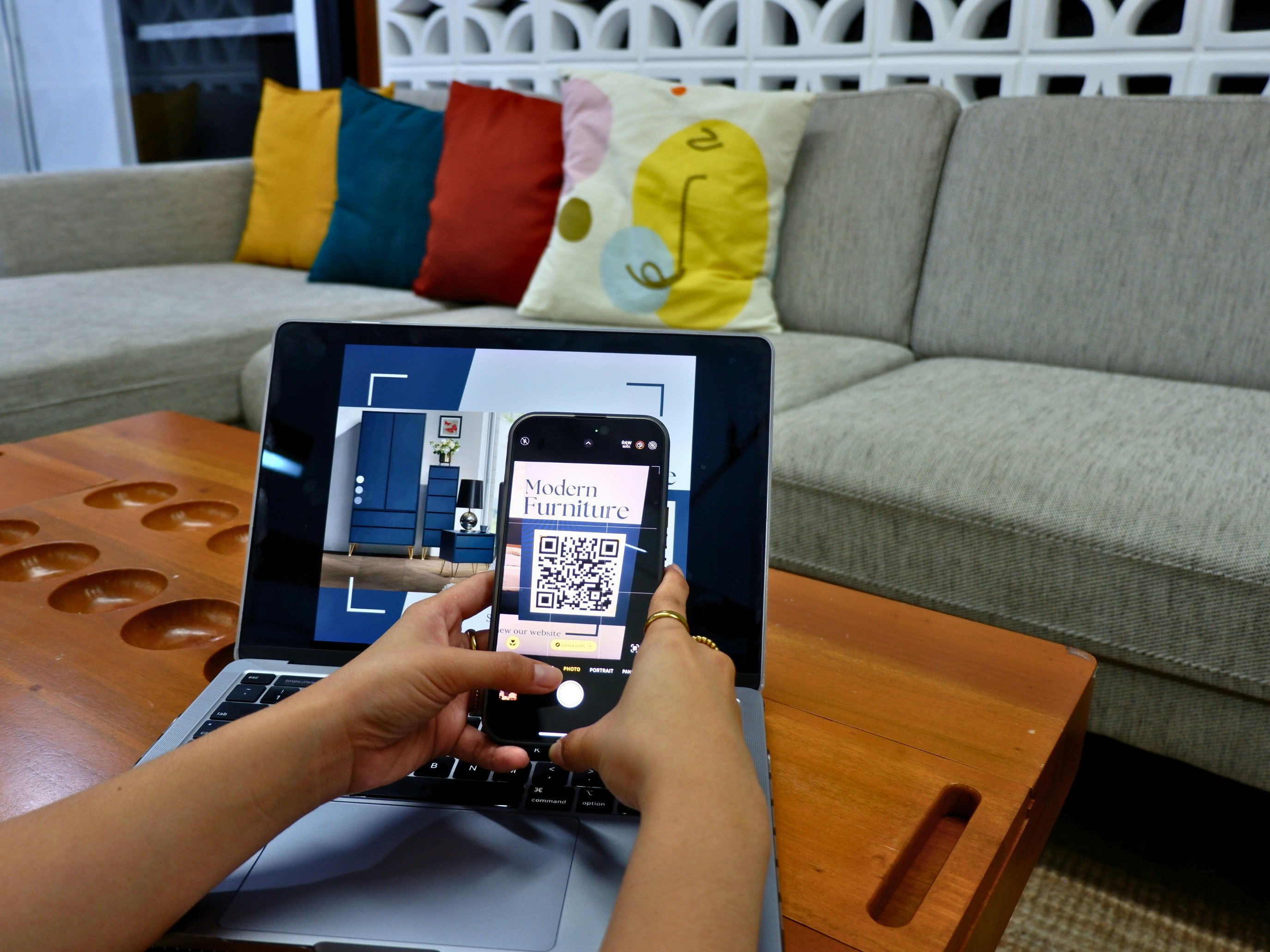 Tangan memegang ponsel untuk memindai kode QR yang tampil di layar laptop.